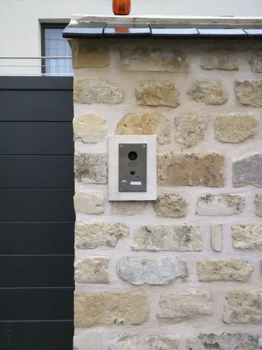 Platine de rue encastrée dans un mur de pierre, à côté d’un portail
