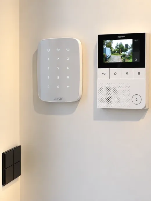 Moniteur DoorBird affichant la vue de la caméra du portier, à côté du clavier d’alarme Ajax dans une entrée